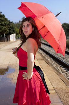 View of a beautiful woman with red dress and umbrella on a train station.