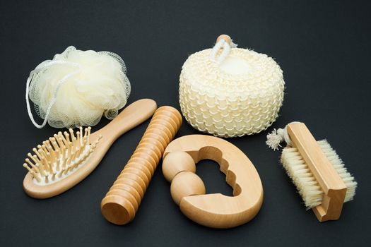 Bath set - massage brush with wooden studs, massage roller, sponge, loofah, nylon tuff on a dark background.