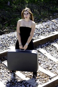 View of a beautiful woman with black dress with a travel case on a train track.