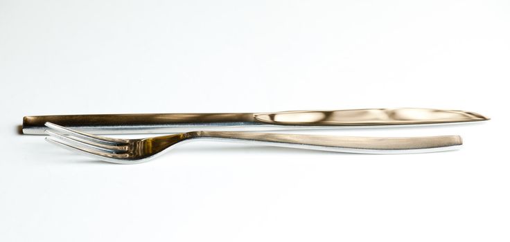 Knive and fork from modern stainless steel design isolated against white and reflecting brown golden light
