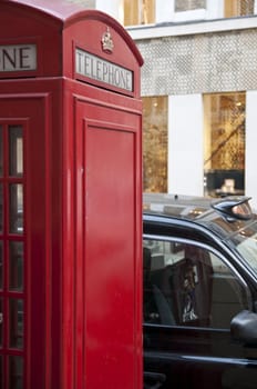 Cropped shot of a traditional red phonebooth with clear side as copy space in London, UK, with black cab parked nearby.