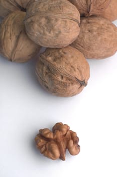 several walnuts on white background, one nut already cracked