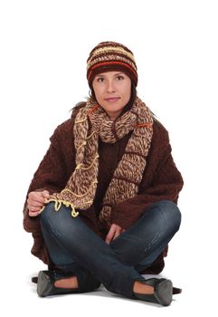 Happy young woman in winter clothes sitting crosslegged against a white background.