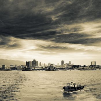 Cityscape of ocean with ship and skyscrapers under dramatic sky in Penang, Malaysia, Asia.