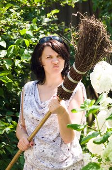 The woman with a broom against a green bush