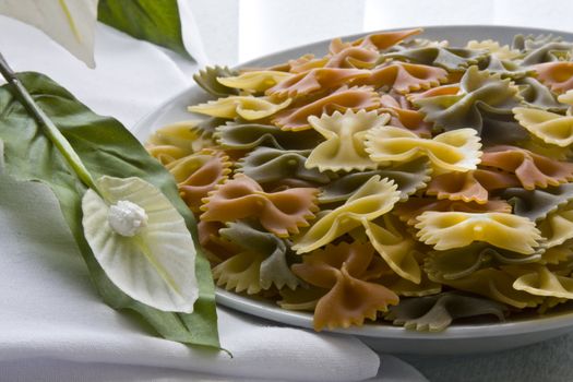 Tricolor farfalle pasta uncooked with flower, bowl and napkin