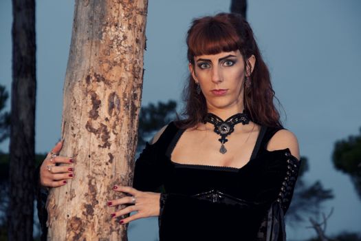Dark gothic woman with dark clothes posing on the night forest.