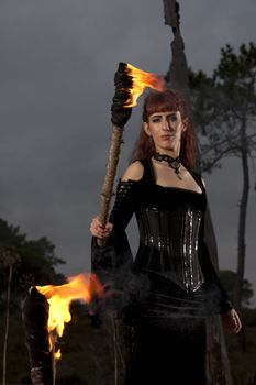 View of a dark clothed woman with a torch on her hands.
