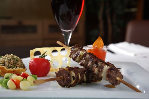Kebab on a white dish with a glass of wine and vegetables