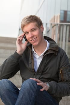 Young happy blond handsome boy holds his mobile phone