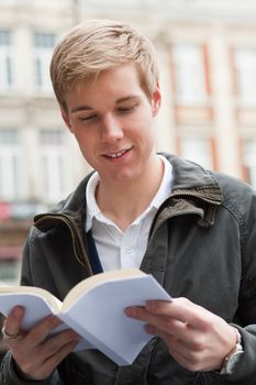 Young cheerful handsome guy reading a book with blank cover