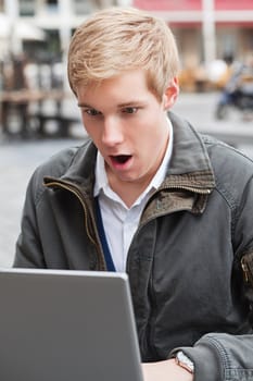 Young handsome man outdoors shocked by information he sees on laptop screen