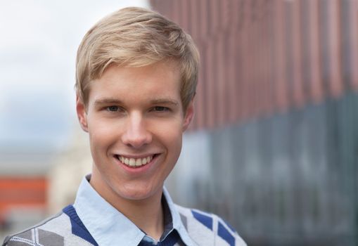 Handsome blond young man smiling outdoors; blurred background