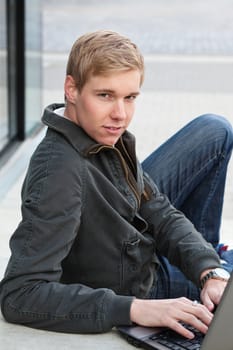 Young blond handsome man with laptop computer in a relaxed pose outdoors