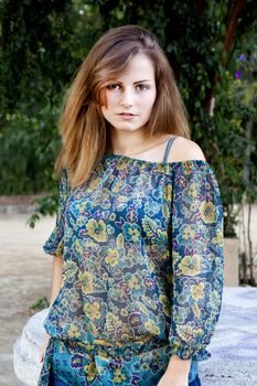 View of a beautiful girl on a floral dress on a park.