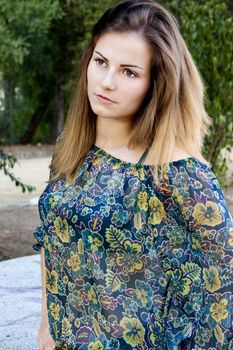 View of a beautiful girl on a floral dress on a park.