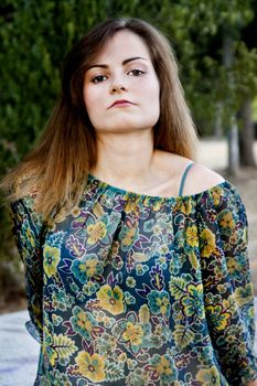 View of a beautiful girl on a floral dress on a park.