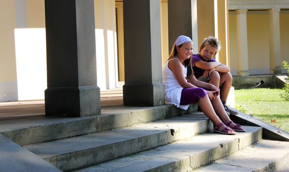 two childrens are sitting in front of an old pathway with pillars