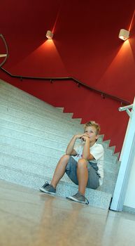 distressed young blonde boy is sitting on the stairs
