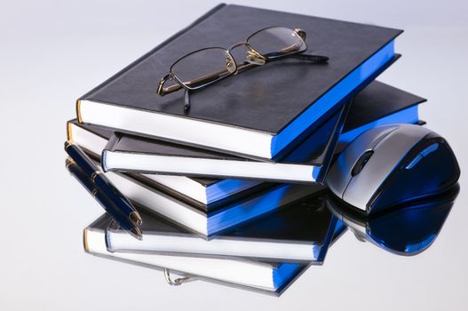 stack of books with pen glasses and a computer mouse