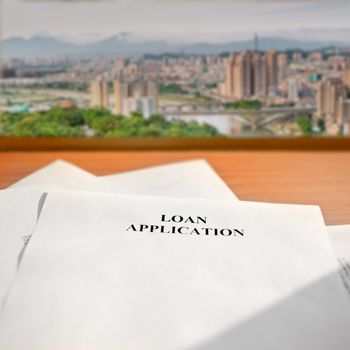 Loan application paper on desk near window and cityscape far away.