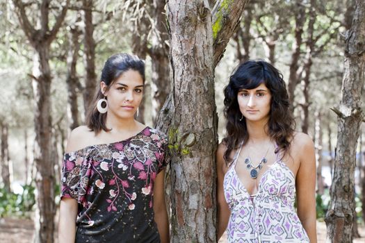 two girls pose next to a tree on the forest