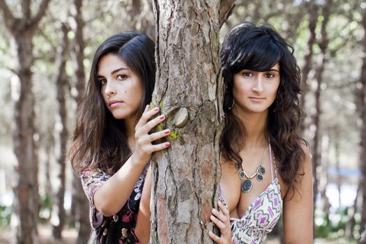 two girls pose next to a tree on the forest