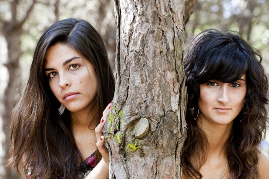 two girls pose next to a tree on the forest