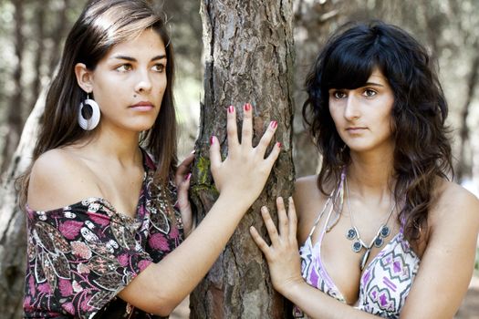 two lovely girls behind a pine tree.