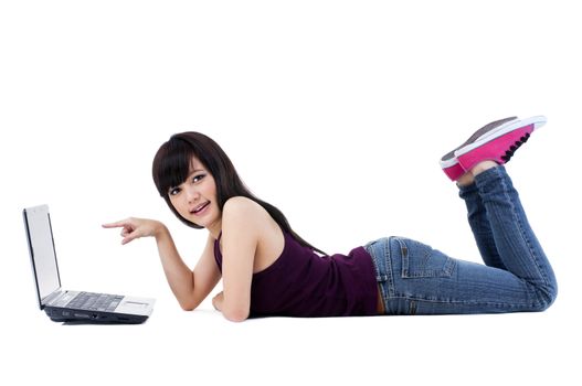 Portrait of a beautiful young woman lying on floor and pointing at her laptop over white background.