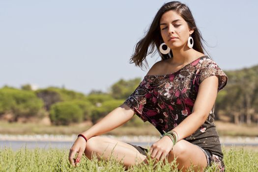Beautiful girl with floral dress meditating on the nature.