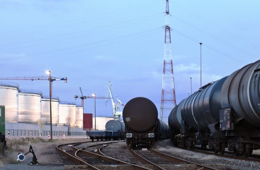 Oil tank cars standing on rail tracks in industrial area; twilight scene