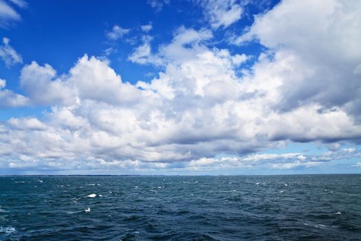 Sea ripples under cloudy sky; sea shore on horizon