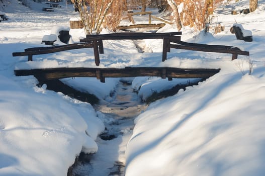 Wooden bridge over small frozen brook. Winter, snow and ice