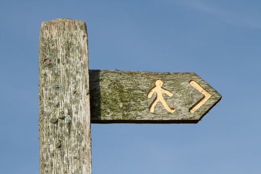 An old wooden sign with a yellow person symbol and arrow against a blue sky.