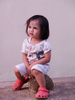 a child is sitting on rock looking dreamily.