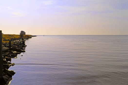 Sunrise on the estuary. Fishermen sit on poles on the shore in the morning