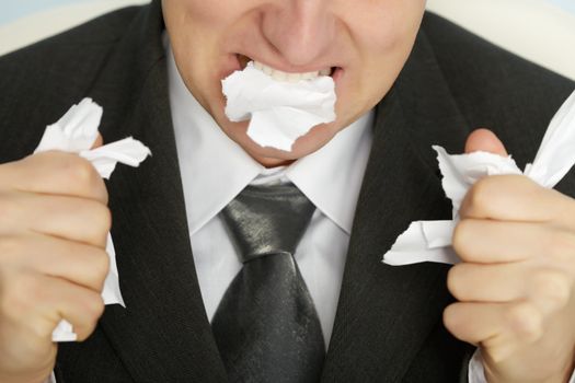 Businessman furiously tearing paper with his teeth and hands