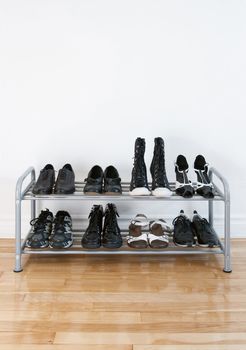 Shoe rack with black shoes and boots, on a wooden floor, besides a white wall.