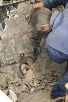 Construction workers hammer away with stones and plaster from a wall
