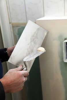 One wall is plastered. A trowel with plaster is held in one hand.
