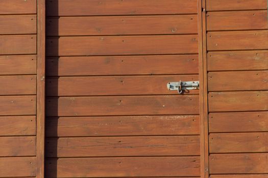 Stained pine slats laying horizontal makes up wood panels with a metal bolt lock.