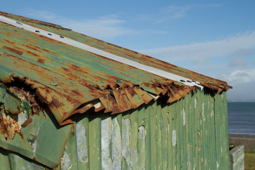 The roof of a tin hut with damaged rusty metal and green flaking paint.