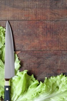 Kitchen knife and green leaves of lettuce lying on wooden surface with copy space