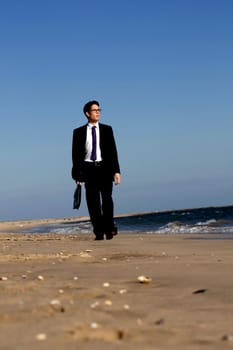 View of a young business man walking down the beach.