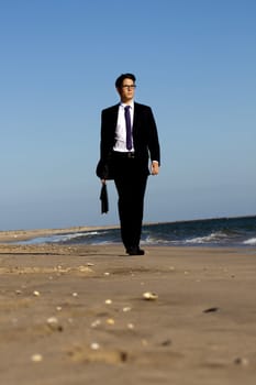 View of a young business man walking down the beach.