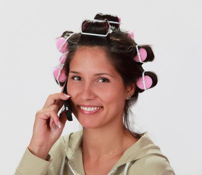 Portrait of a smiling young woman with hair curlers using a mobile phone.