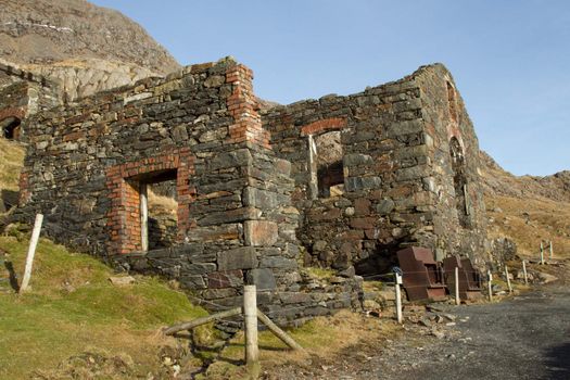 The derelict ruins of an historical copper mine with a protective fence and mountain in the high distance.