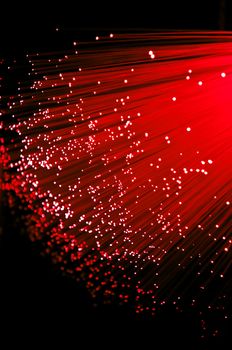 Close up on ends of many illuminated red fibre optic strands with black background.