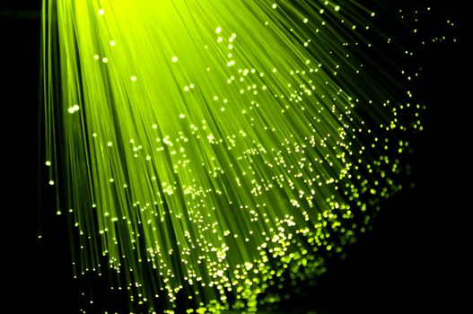 Close up on ends of many illuminated fibre optic strands with black background.